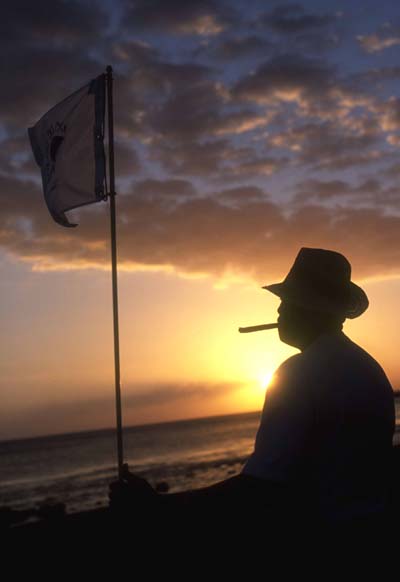 A golfer enjoys a Dominican cigar at sunset on the 5th green at the Teeth of the Dog (Photography by Paul Marshall)
