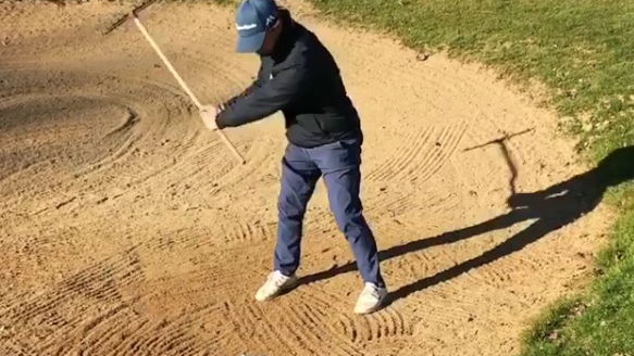 golfer uses bunker rake to hit shot out of sand
