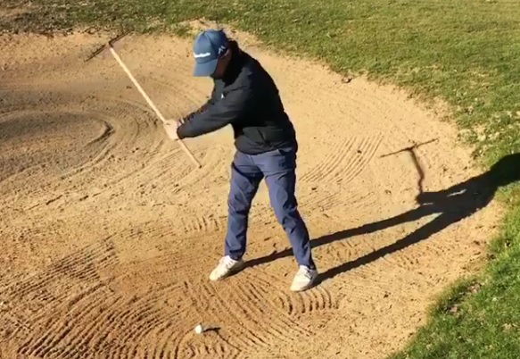 golfer uses bunker rake to hit shot out of sand