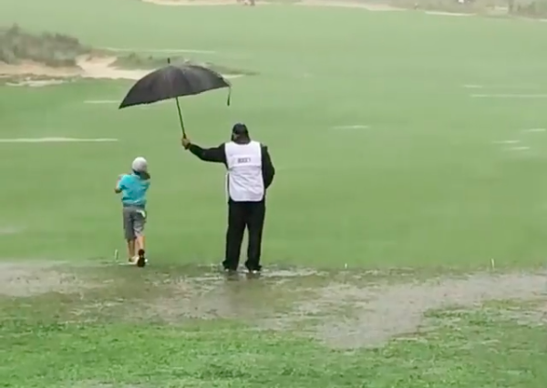 WATCH: Caddie protects young golfer from TORRENTIAL weather conditions